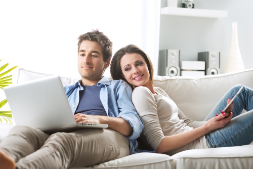 Young couple relaxing on sofa with digital tablet and laptop.