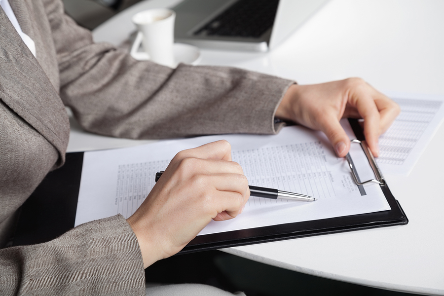 Hand of a businesswoman at her desk with a pen and a clipboard