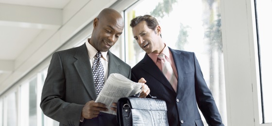 Multi ethnic businessmen reading newspaper together in office